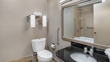 A bathroom with a toilet, sink, mirror, towel rack, and grab bars.