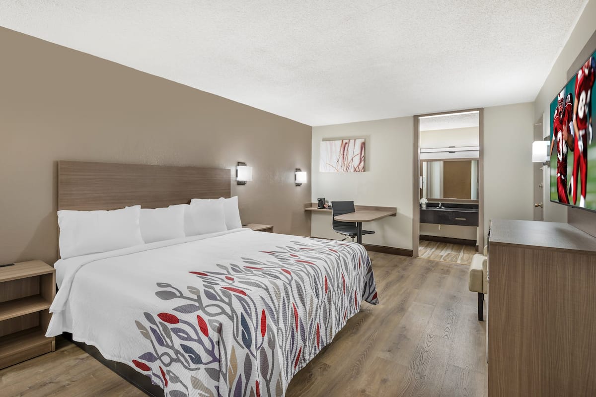 A hotel room with a bed, a desk, a chair, a TV, and a bathroom.