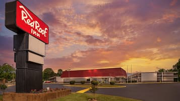 A Red Roof Inn with a large sign, a parking lot, and a building with a red roof.