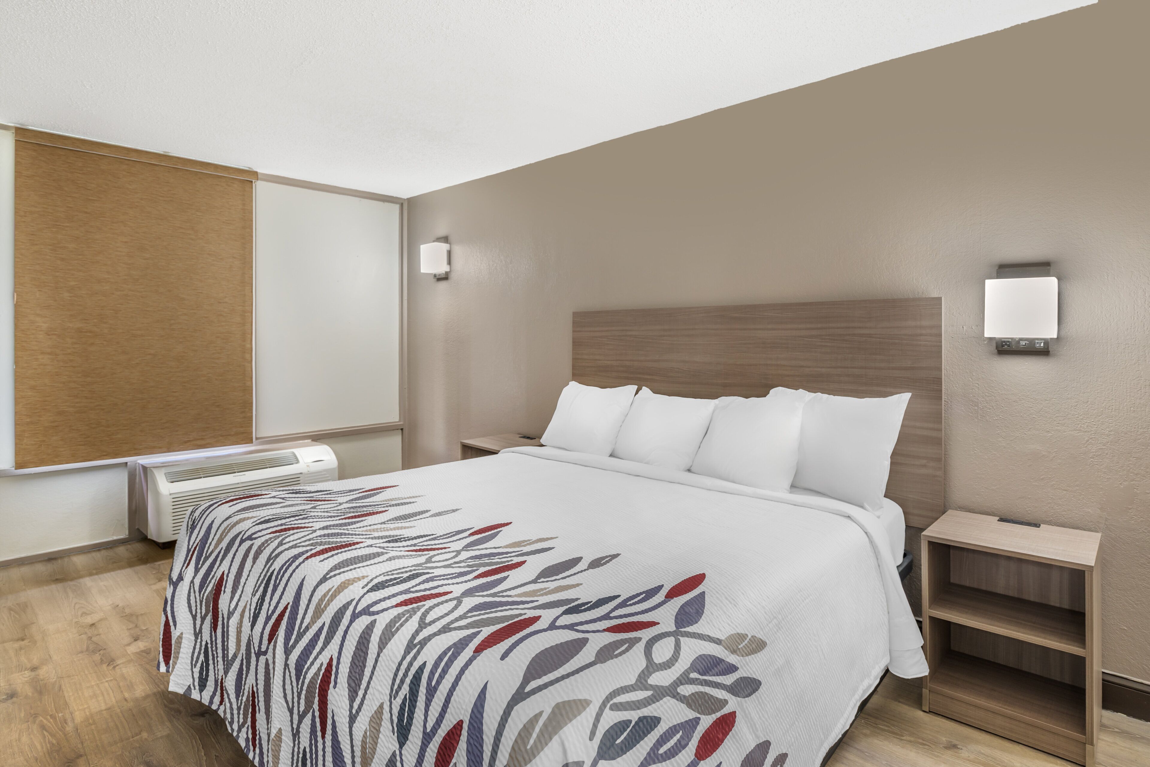 A hotel room with a bed, bedside tables, a heater, and a wall-mounted light fixture.