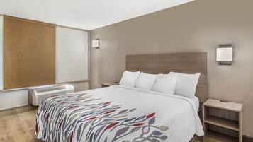 A hotel room with a bed, bedside tables, a heater, and a wall-mounted light fixture.