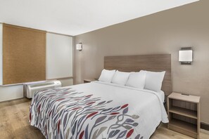 A hotel room with a bed, bedside tables, a heater, and a wall-mounted light fixture. - Red Roof Inn Richmond, VA (Richmond)