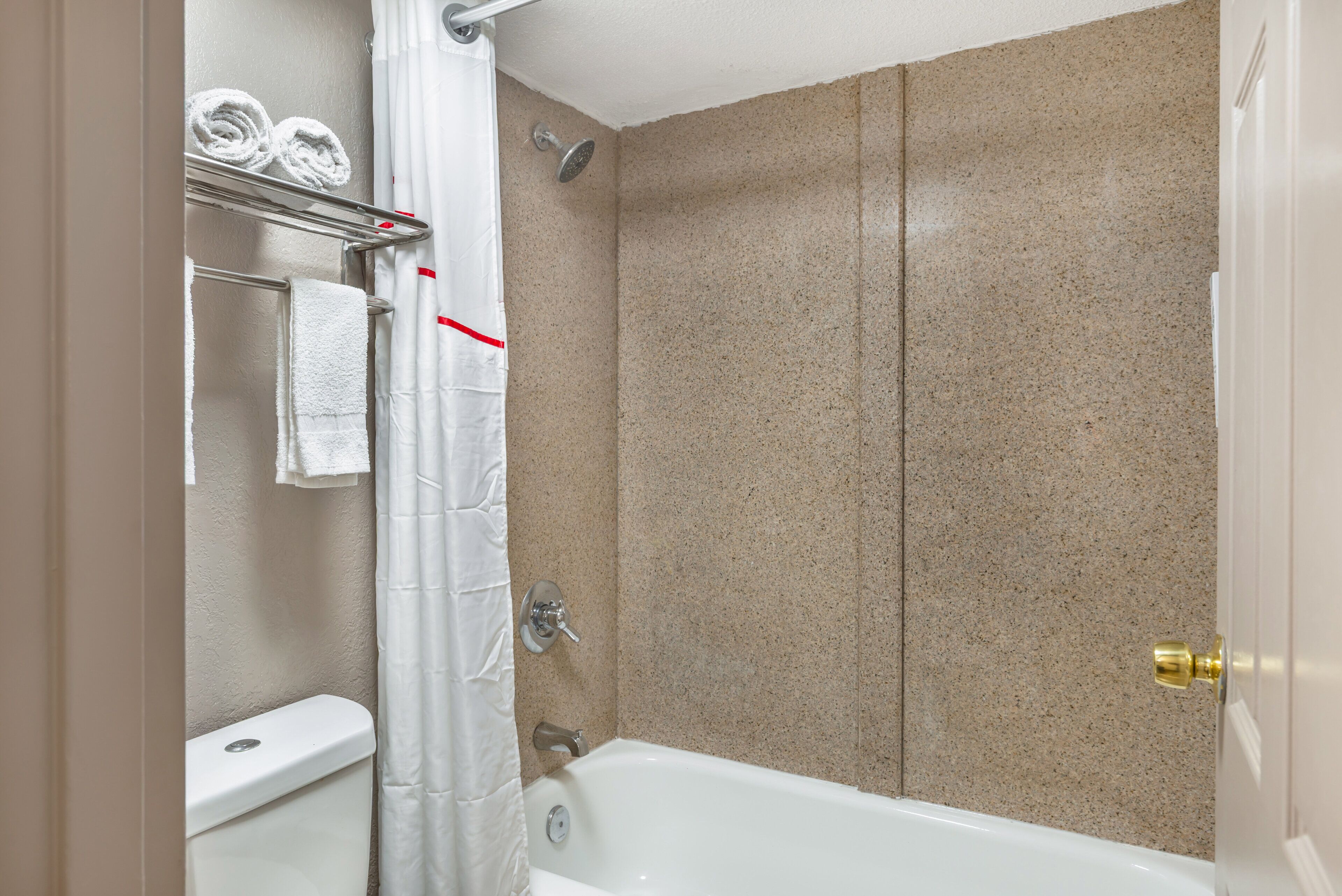 Une salle de bain avec une baignoire, une douche et des toilettes. On y trouve des serviettes et un rideau de douche.