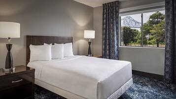 Una habitación de hotel con una cama grande, dos mesitas de noche, una ventana con vistas a un puente y una alfombra estampada.