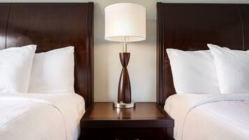 Habitación de hotel con dos camas, una mesita de noche con lámpara y un cajón.