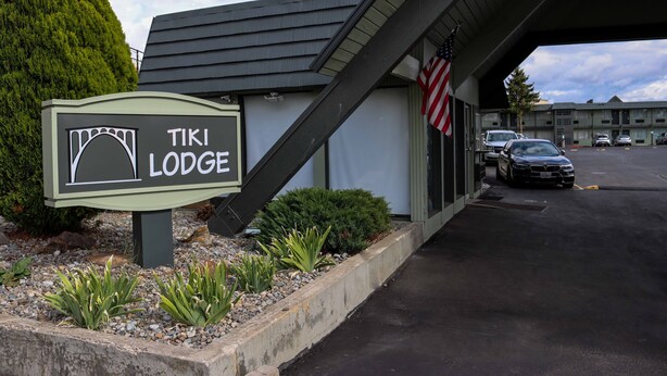 Een TIKI Lodge bord met een tent symbool, een parkeerplaats met auto's, en een Amerikaanse vlag.