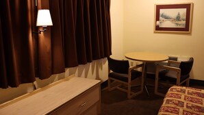 Een hotelkamer met een bed, een bureau, een stoel, een tafel, een lamp en een schilderij aan de muur.