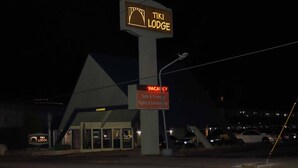 Een TIKI LODGE bord met daaronder een 'VACANCY' bord, wat aangeeft dat er kamers beschikbaar zijn.
