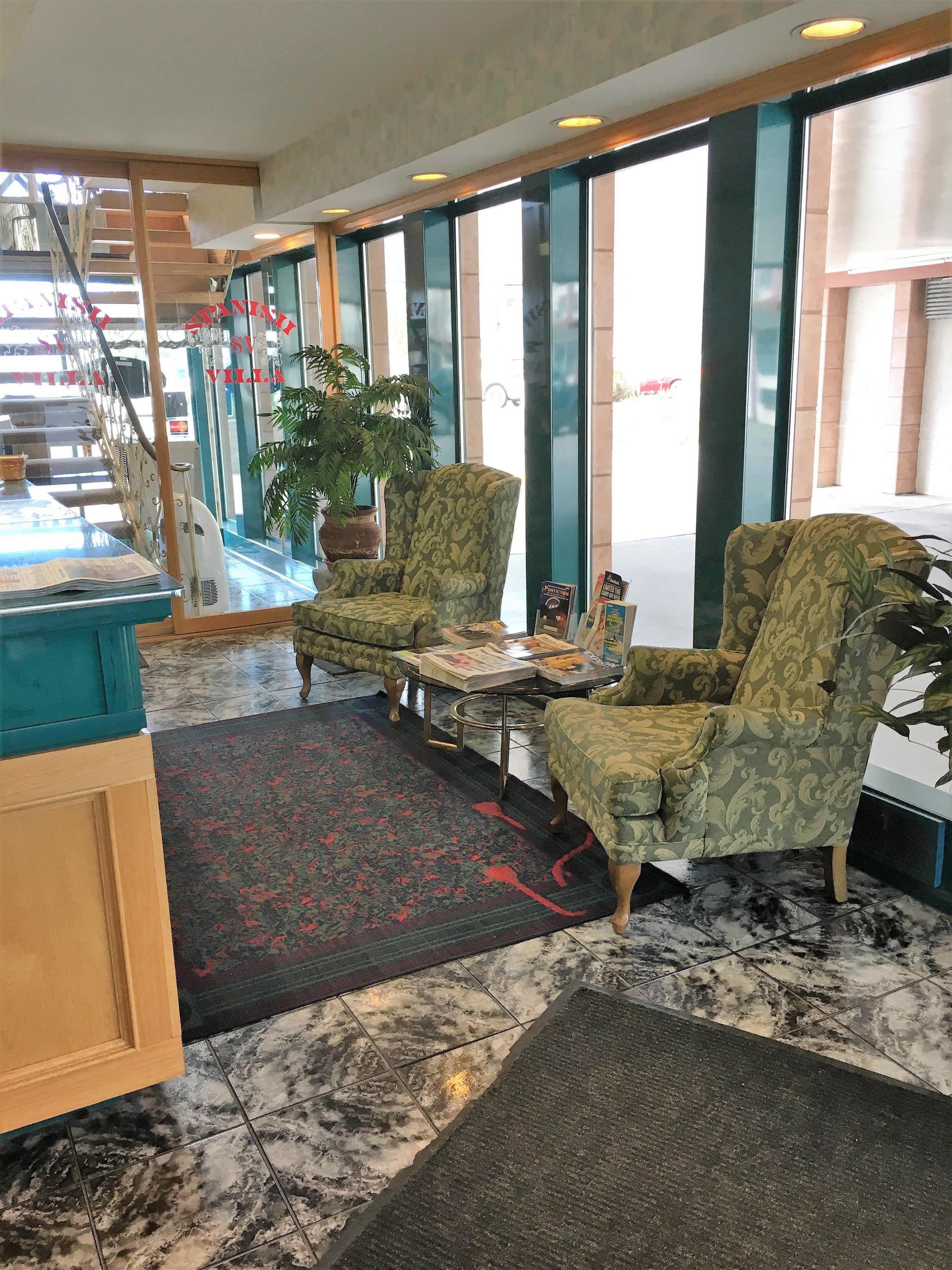 A lobby with a reception desk, two patterned armchairs, a coffee table, a potted plant, and a staircase.