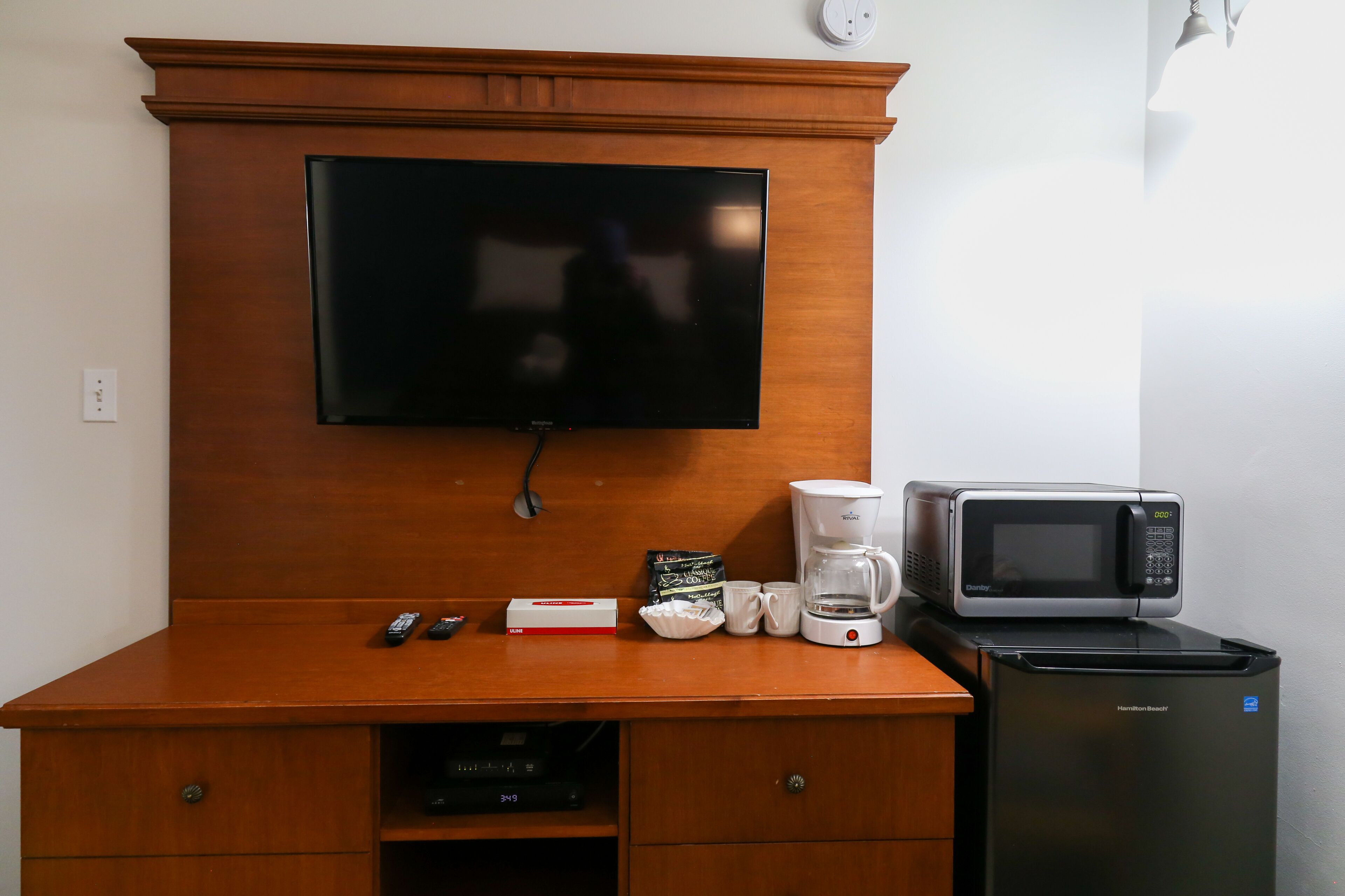 A wooden desk with a flat-screen TV, a microwave, a coffee maker, and a refrigerator.