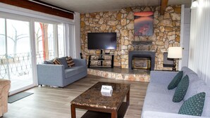 A living room with a stone wall, a fireplace, a flat-screen TV, a sofa, and a coffee table. - Spanish Villa Resort (Penticton)