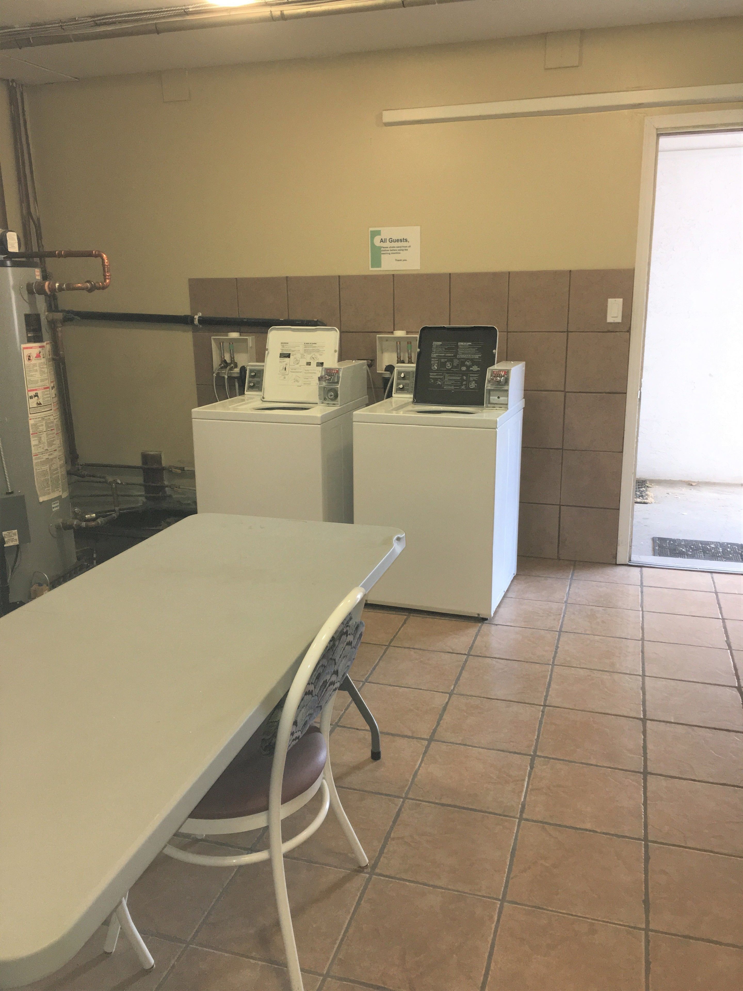A laundry facility with two washing machines, a table, and a sign for guests.