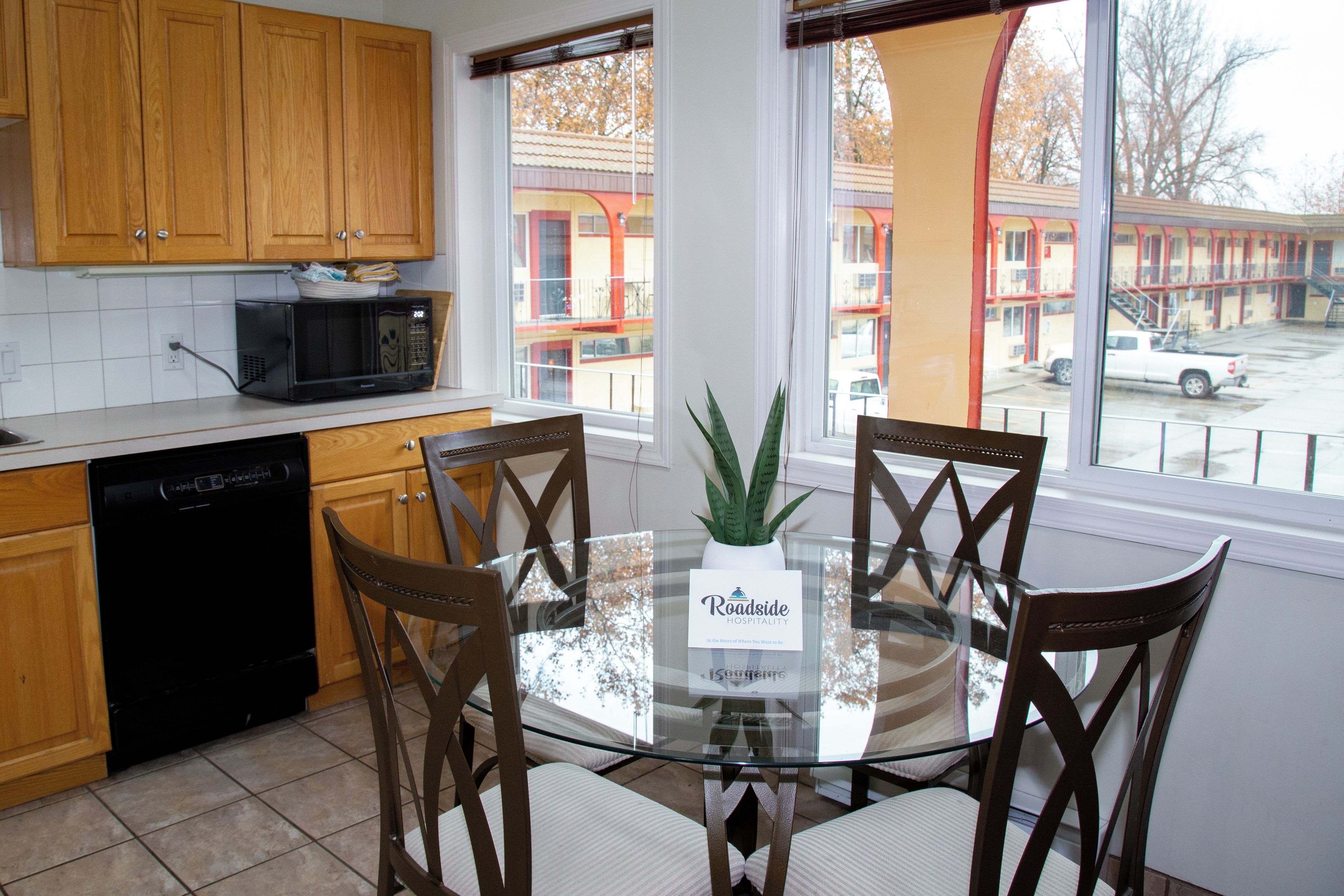 Una cocina con armarios de madera, un microondas, un lavavajillas y una mesa de comedor con sillas. Hay una ventana con vistas a edificios.