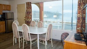 A dining area with a round table and six chairs, a kitchen with a refrigerator and stove, and a large window with a view of the outdoors. - Spanish Villa Resort (Penticton)