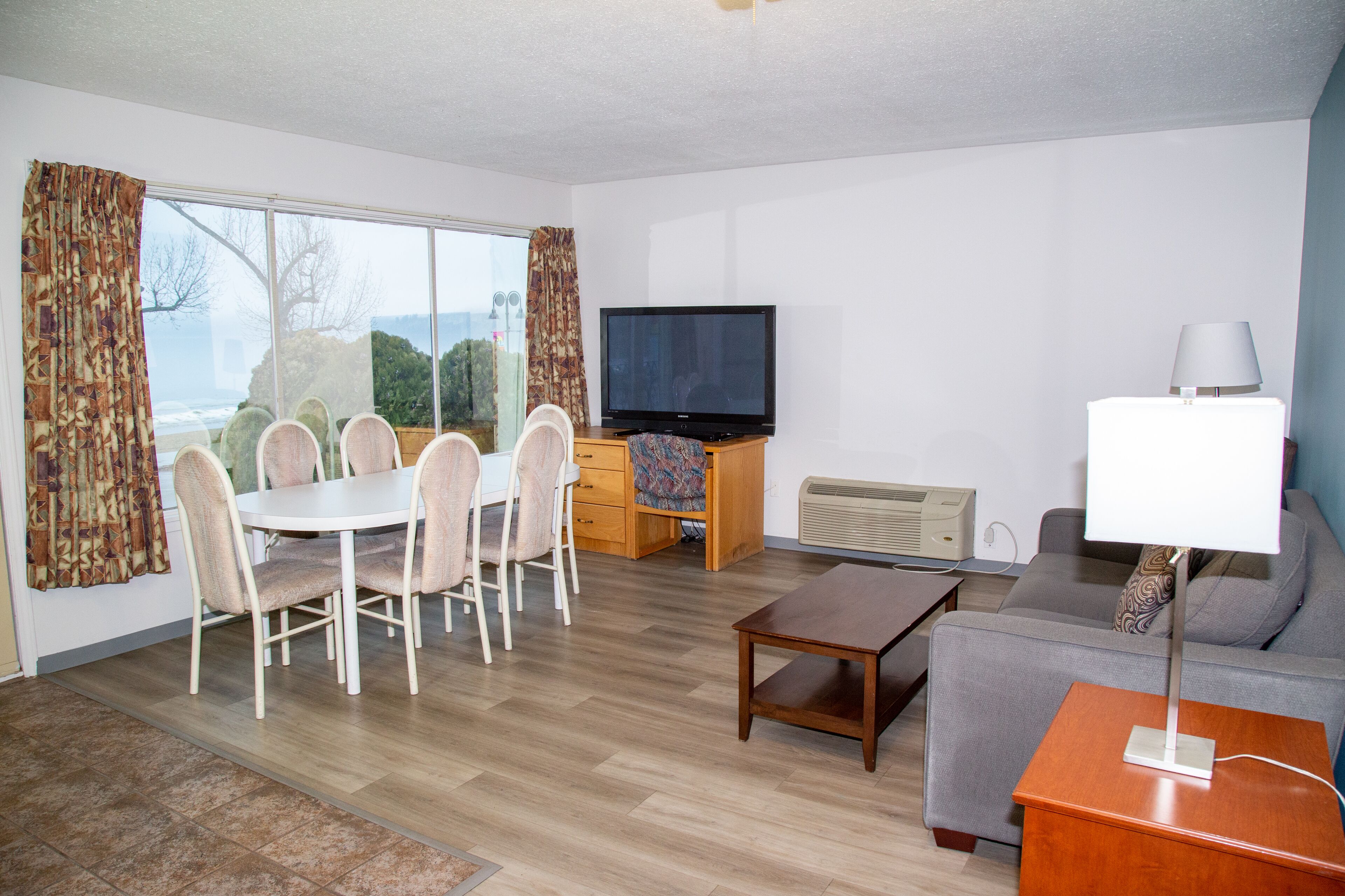 A living room with a dining table, chairs, a sofa, a TV, and a lamp.