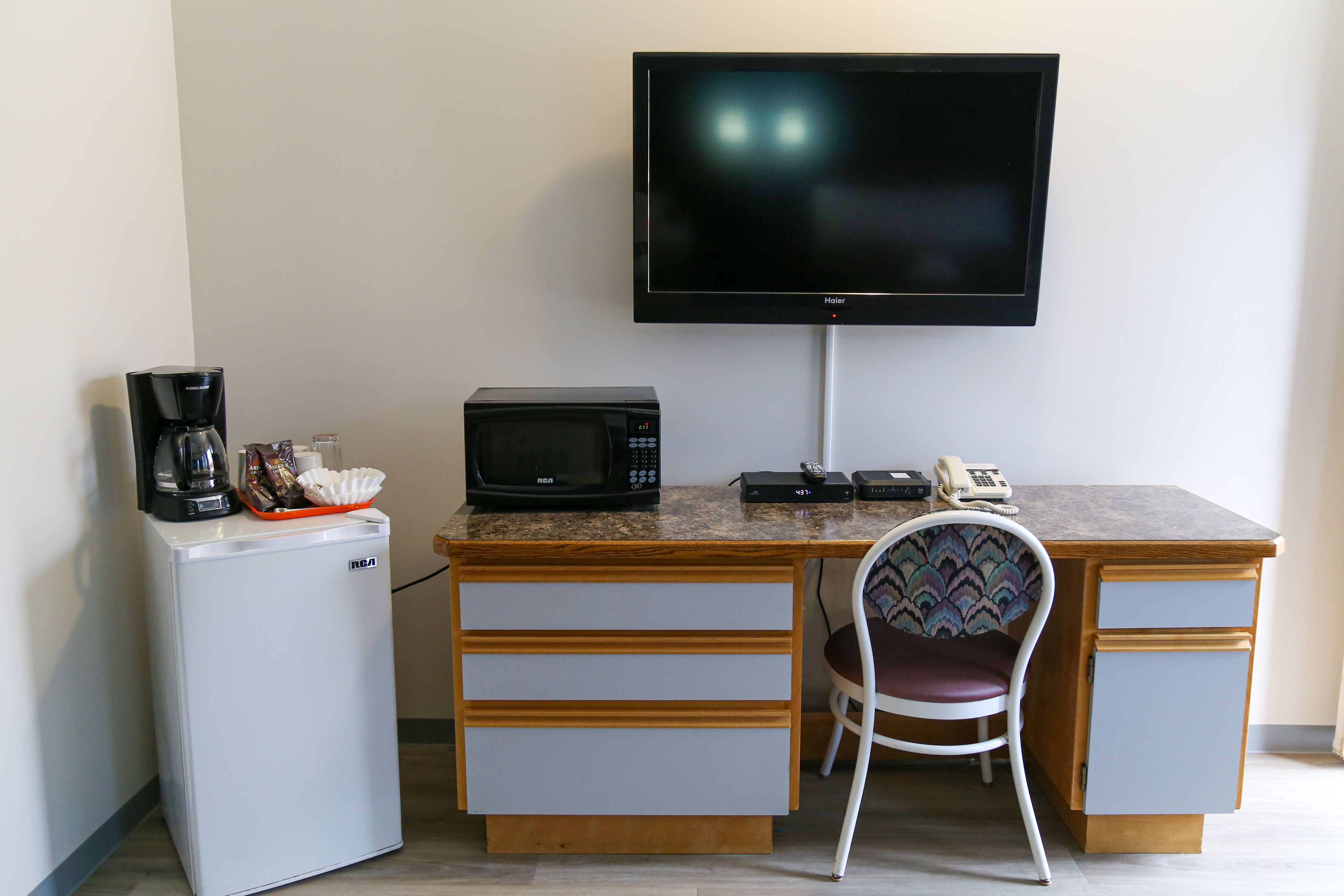 A compact kitchenette with a refrigerator, microwave, coffee maker, and a flat-screen TV mounted on the wall.