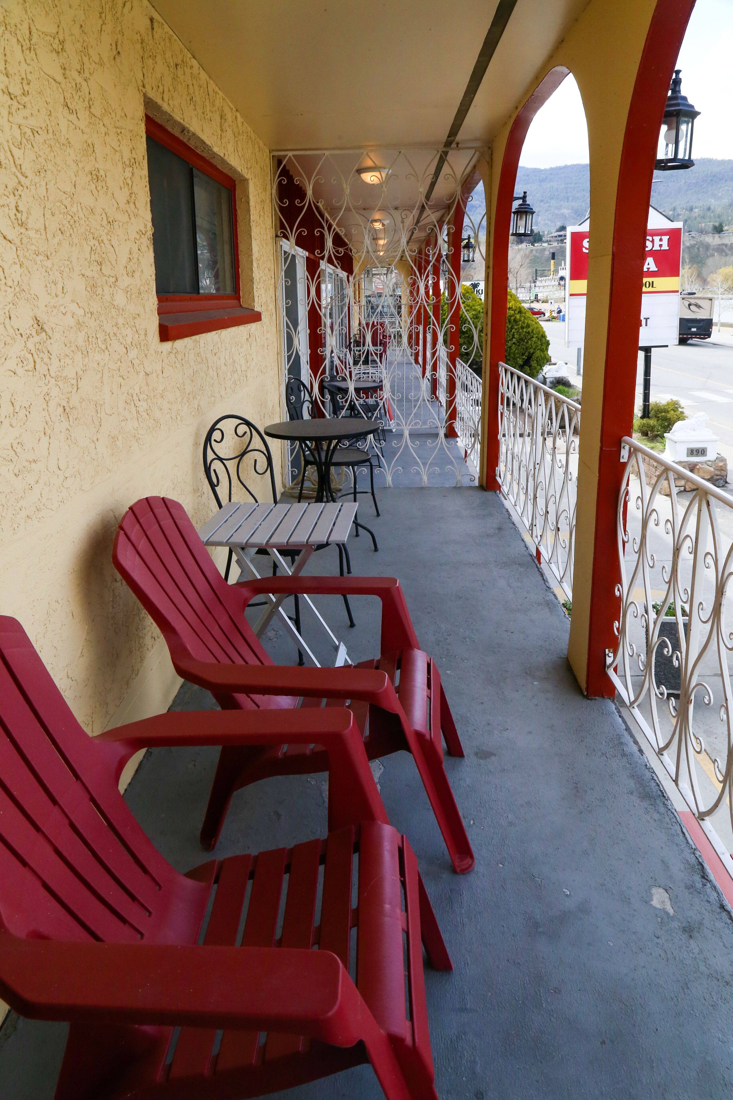 A covered outdoor seating area with red chairs and tables, a window with a red frame, and a view of a mountain in the background.