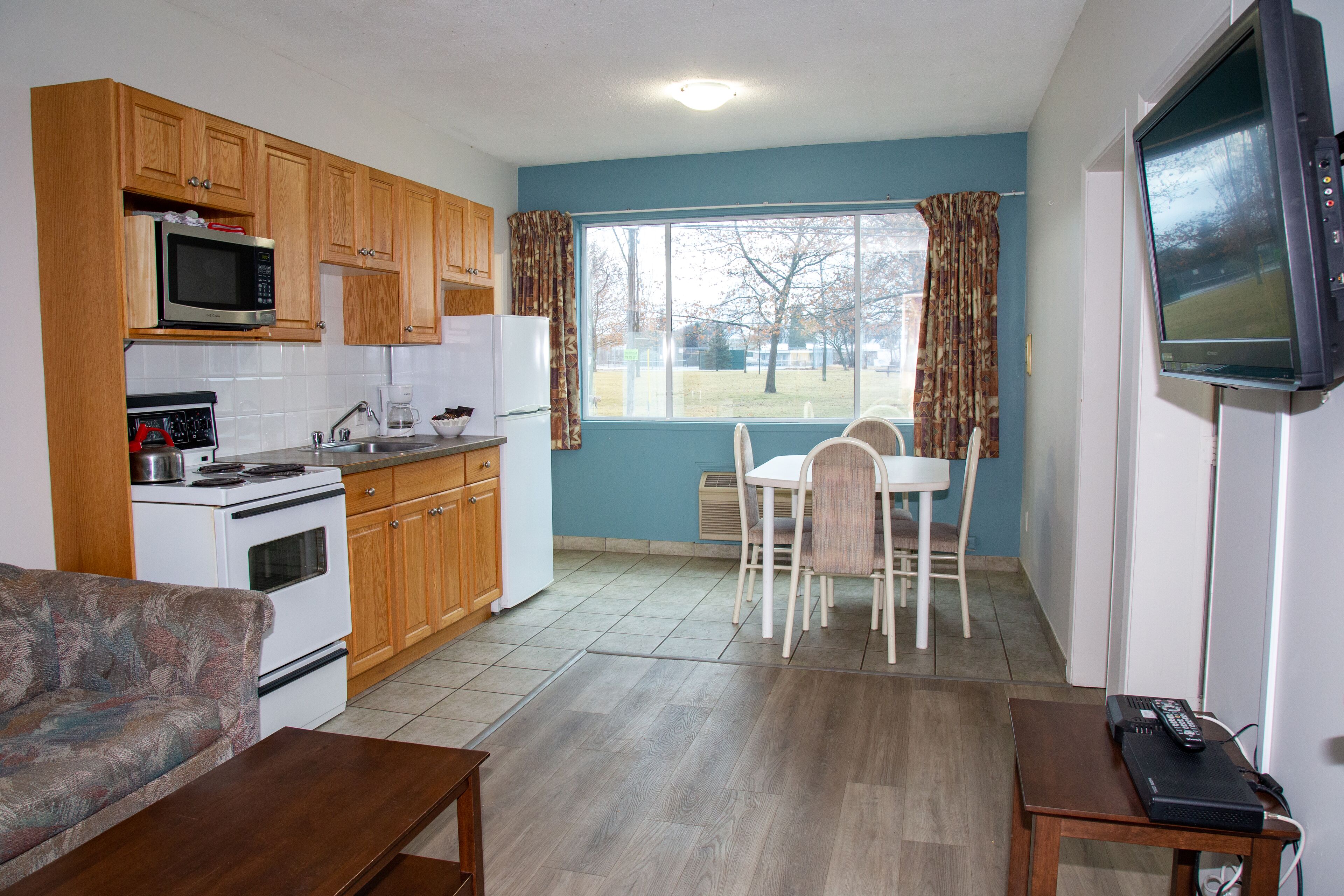 Cocina compacta con armarios de madera, microondas, estufa y comedor con mesa y sillas.