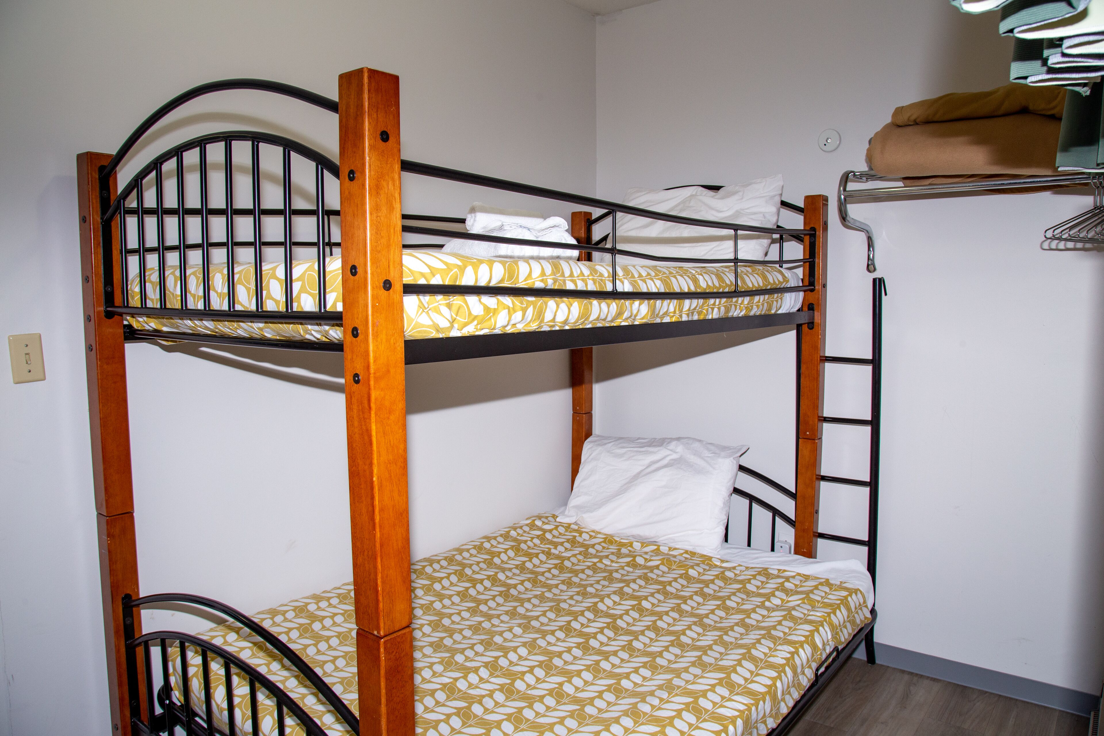 Ein Stockbett mit gemustertem Bettbezug, Holzrahmen und einem Metall-Kopfstück.