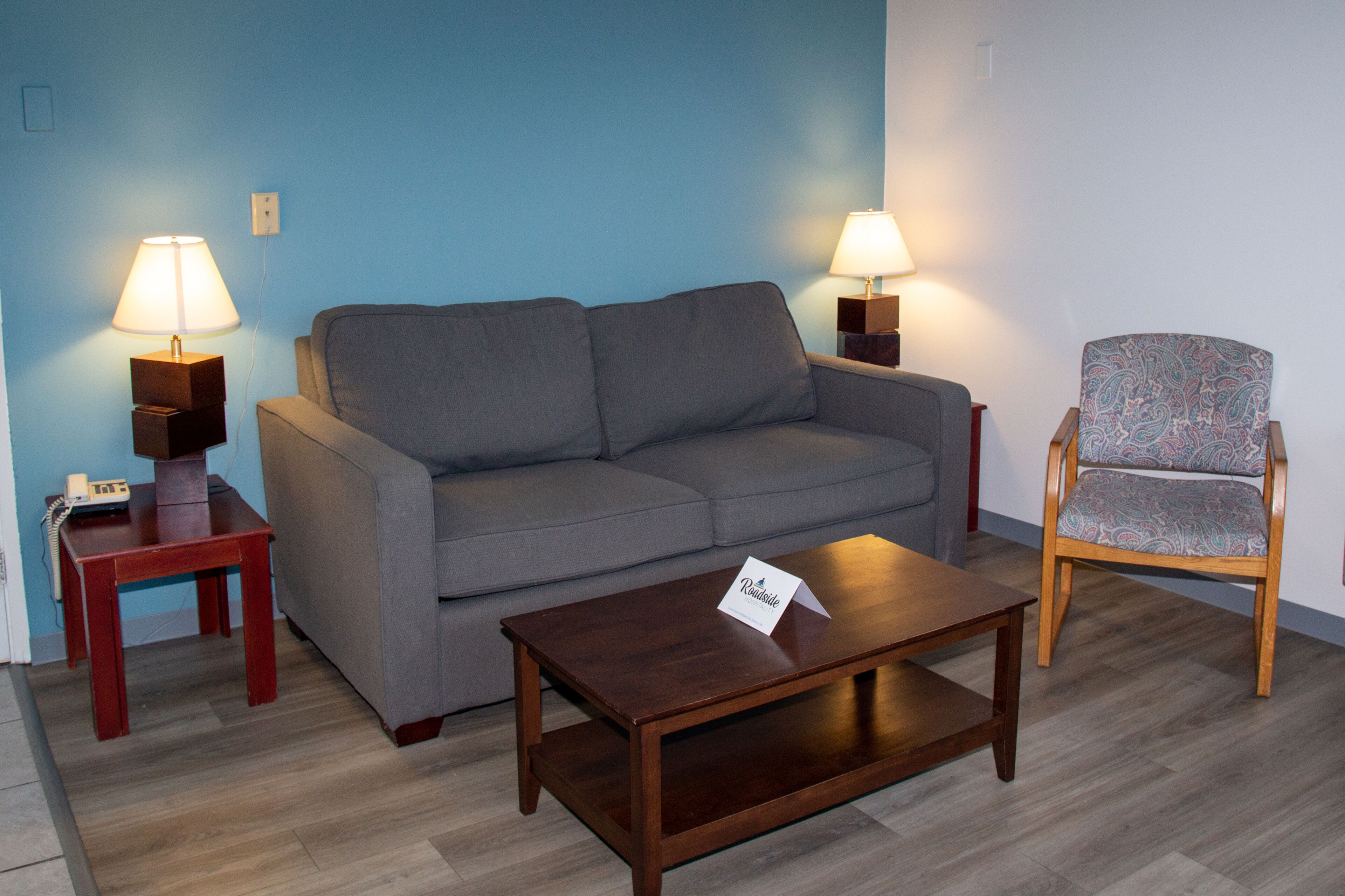 A living room with a grey sofa, a wooden coffee table, a patterned armchair, and two bedside lamps.