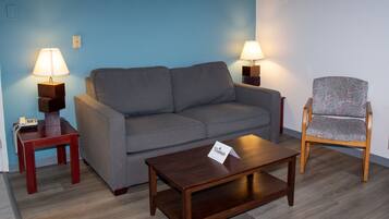 Una sala de estar con un sofá gris, una mesa de centro de madera, un sillón estampado y dos lámparas de noche.