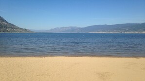 A beach with a clear view of the water and distant mountains. - Spanish Villa Resort (Penticton)