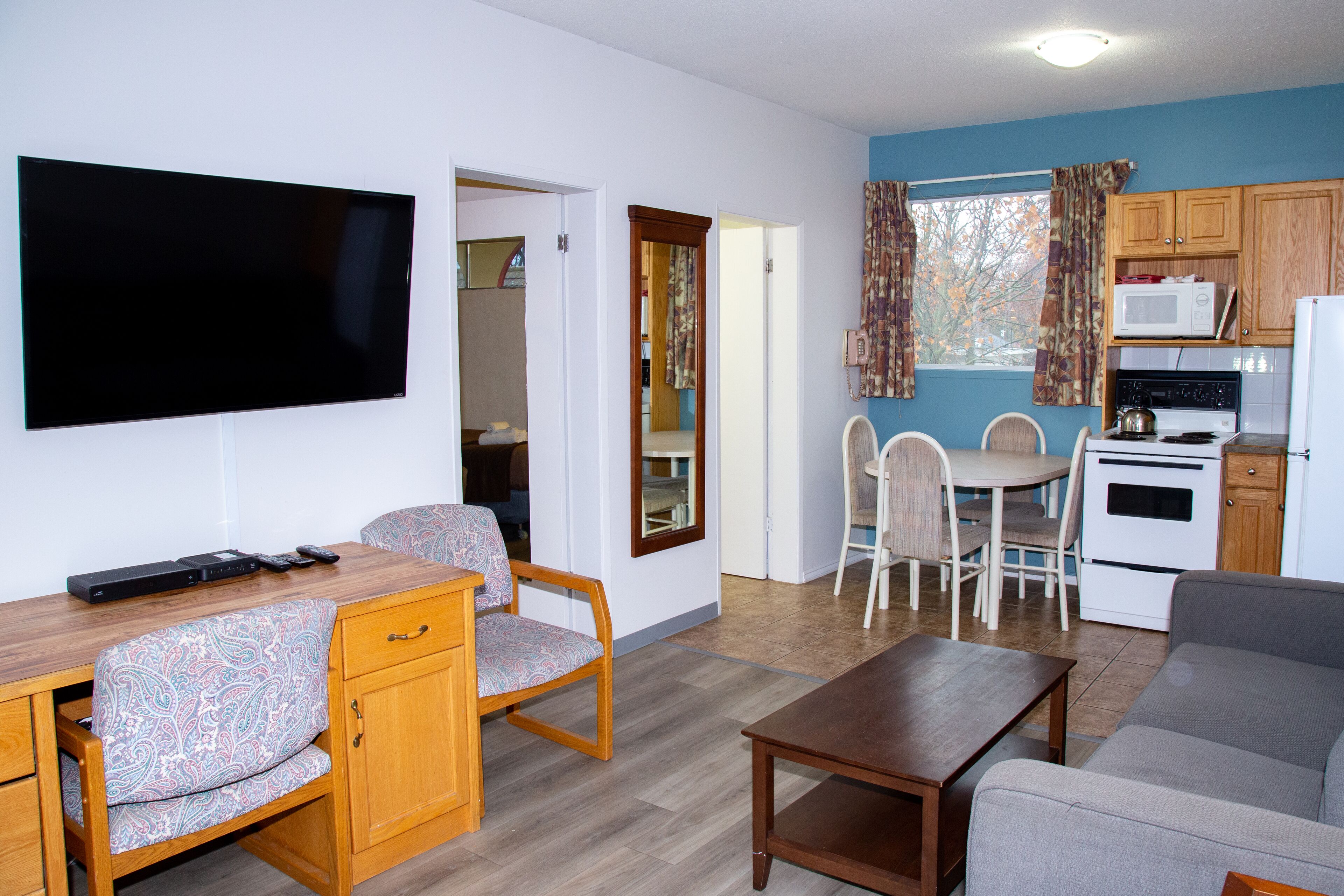 A living room with a flat-screen TV, wooden furniture, a sofa, and a kitchen area with a microwave and stove.