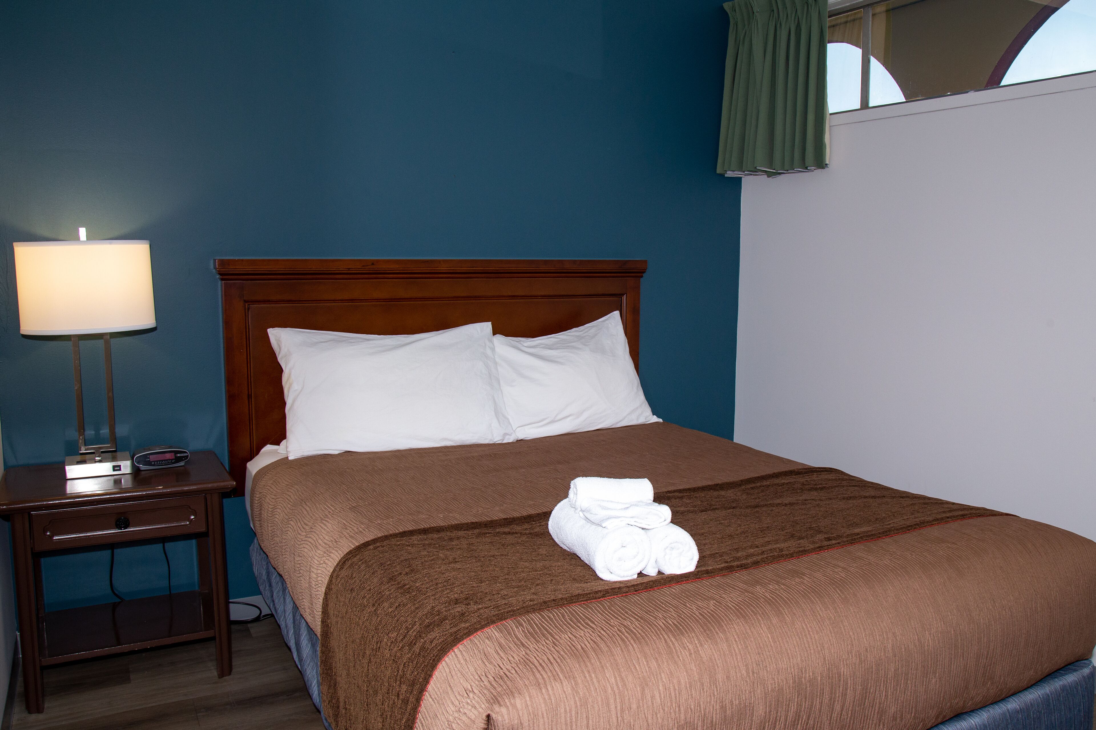 A neatly made bed with a brown bedspread and white pillows, a bedside lamp, and a small nightstand with a lamp.
