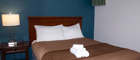 A neatly made bed with a brown bedspread and white pillows, a bedside lamp, and a small nightstand with a lamp.
