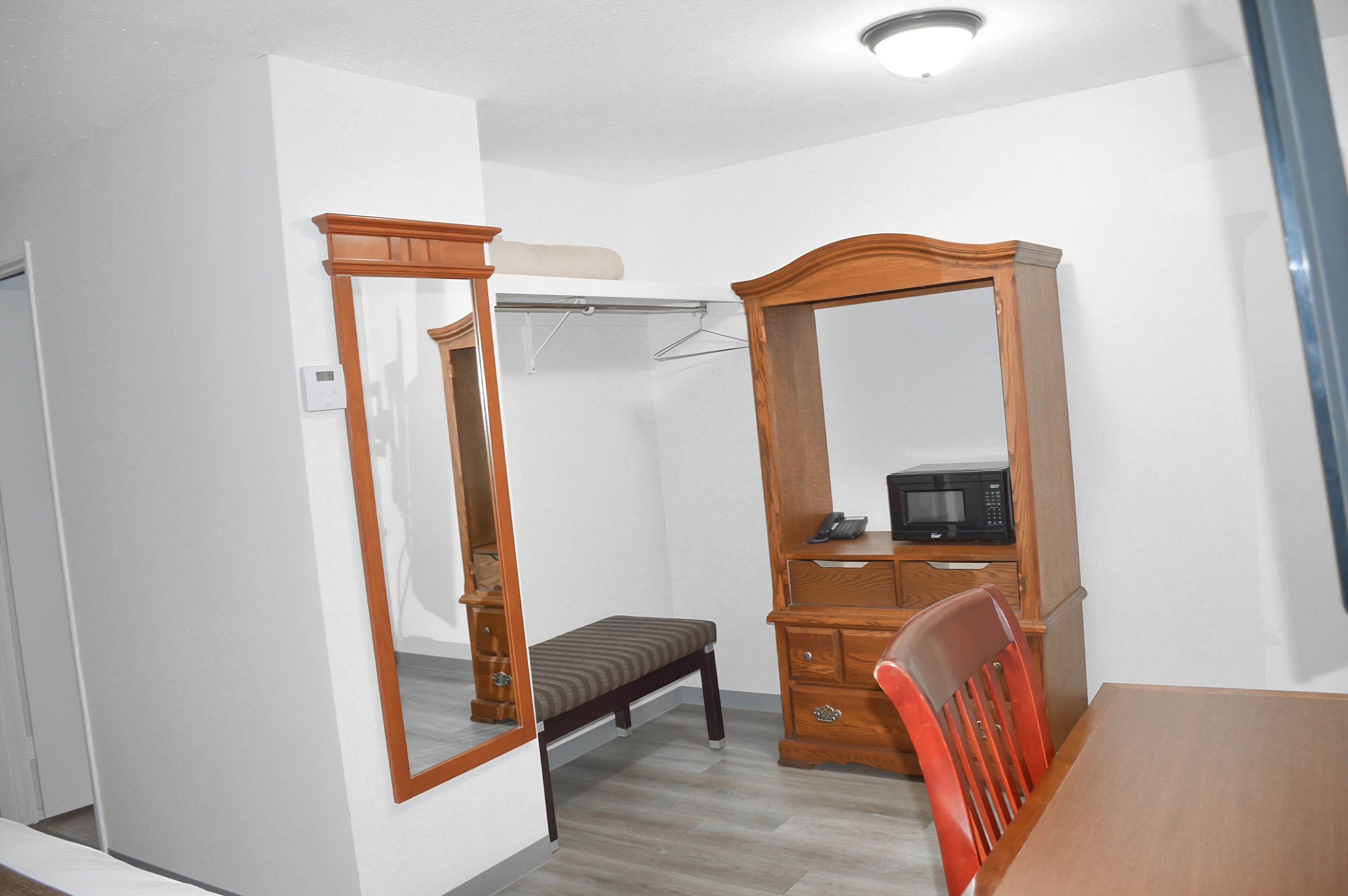 A bedroom with a wooden wardrobe, a bedside table, a chair, and a hanging clothes rack.