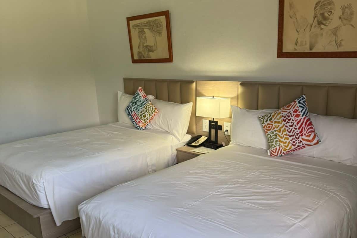 A hotel room with two beds, a nightstand, a lamp, and two framed pictures on the wall.