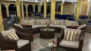 Un amplio salón con sofás y sillones de mimbre, una mesa de centro de vidrio y un jarrón decorativo.