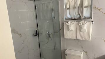 Un baño con ducha envuelta en vidrio, inodoro y un perchero con dos toallas.