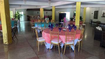 A spacious hall with round tables and chairs, a chandelier, and a large window.