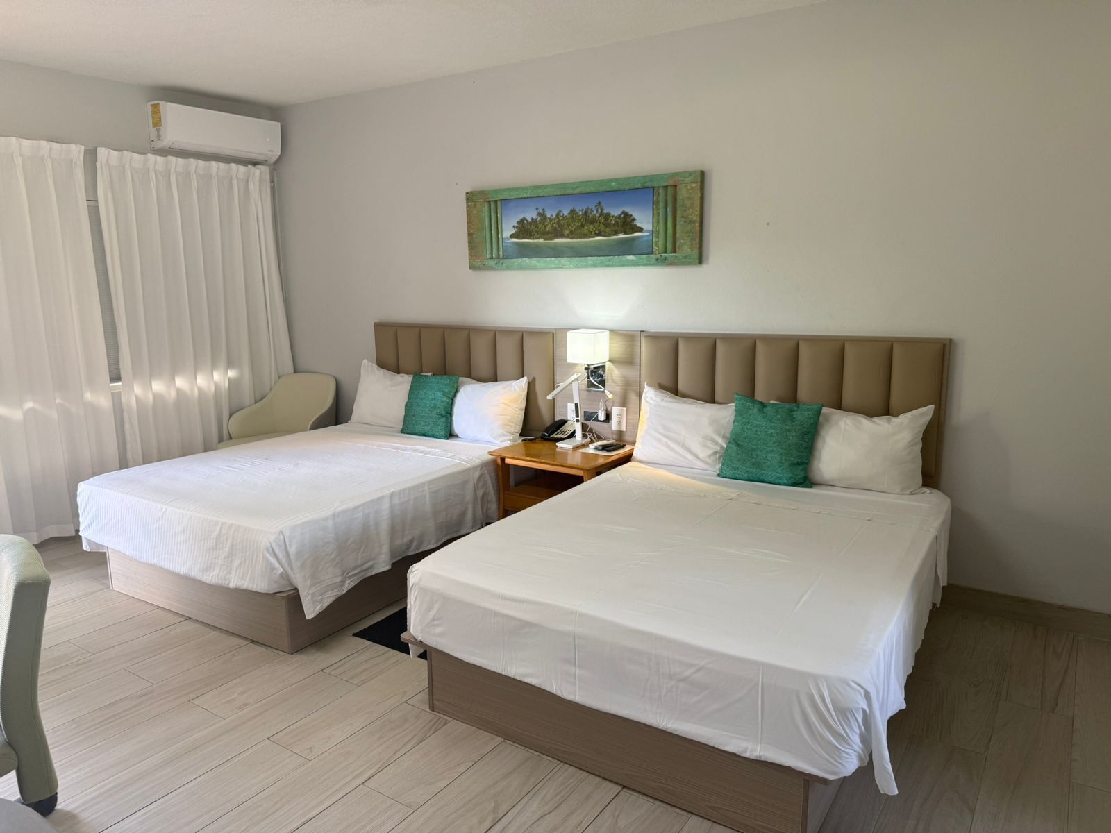 A hotel room with two beds, a nightstand, a lamp, a painting, and a window with curtains.