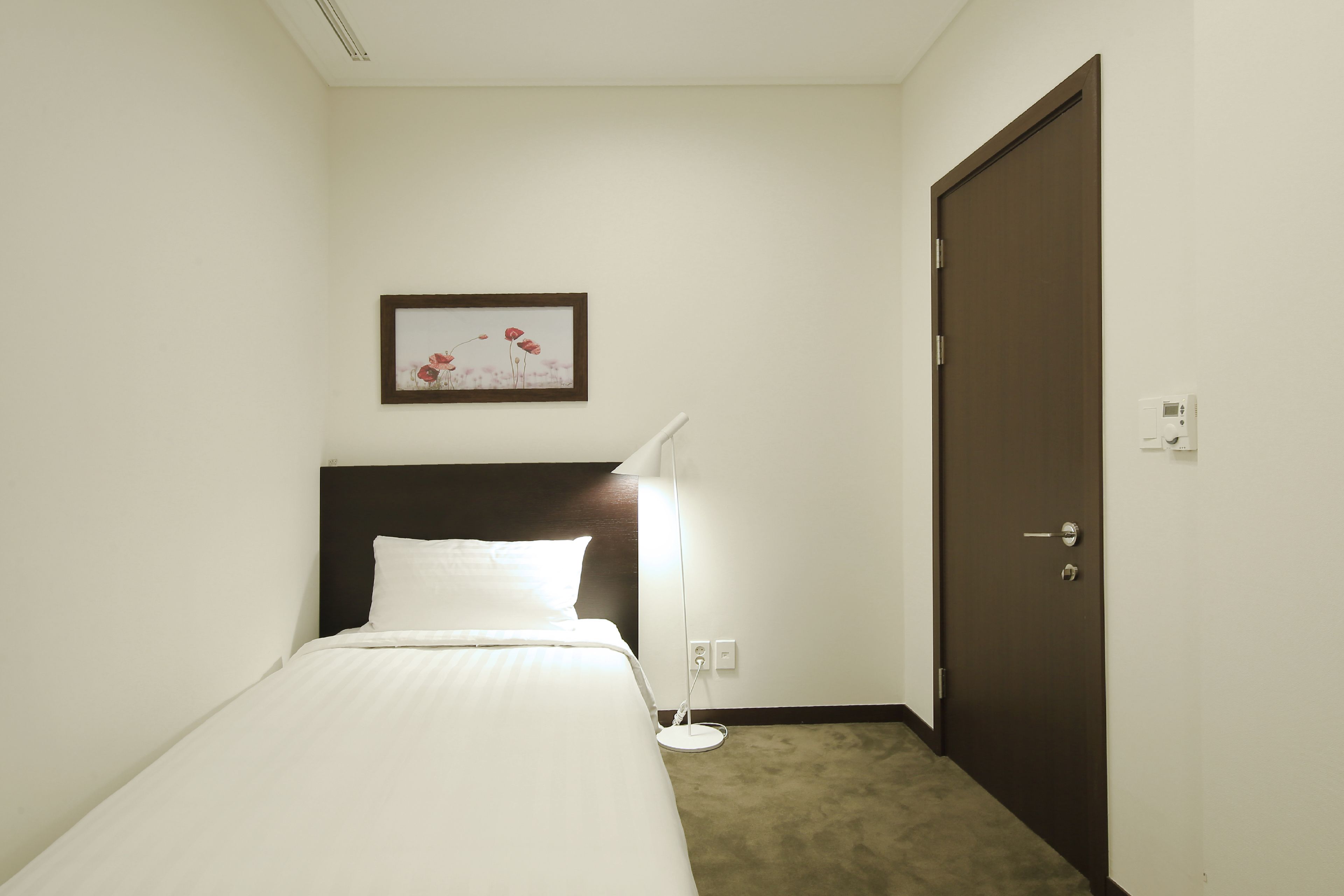 A hotel room with a bed, a bedside lamp, a door, and a framed picture on the wall.