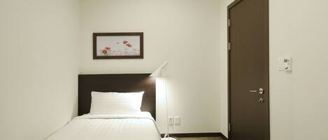 A hotel room with a bed, a bedside lamp, a door, and a framed picture on the wall.