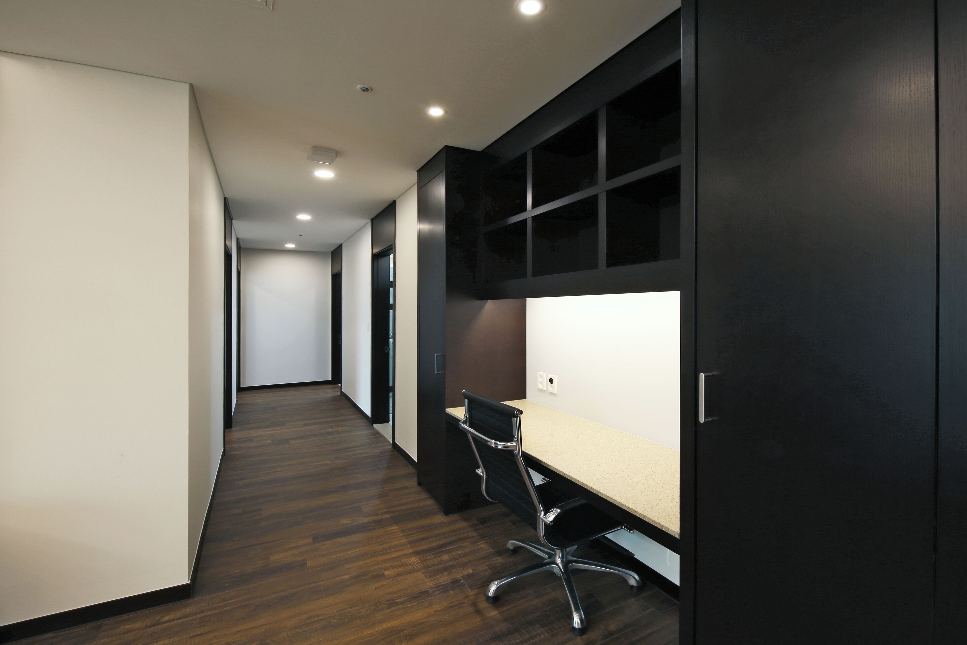 A modern office space with a long corridor, a desk with a chair, and built-in shelving.