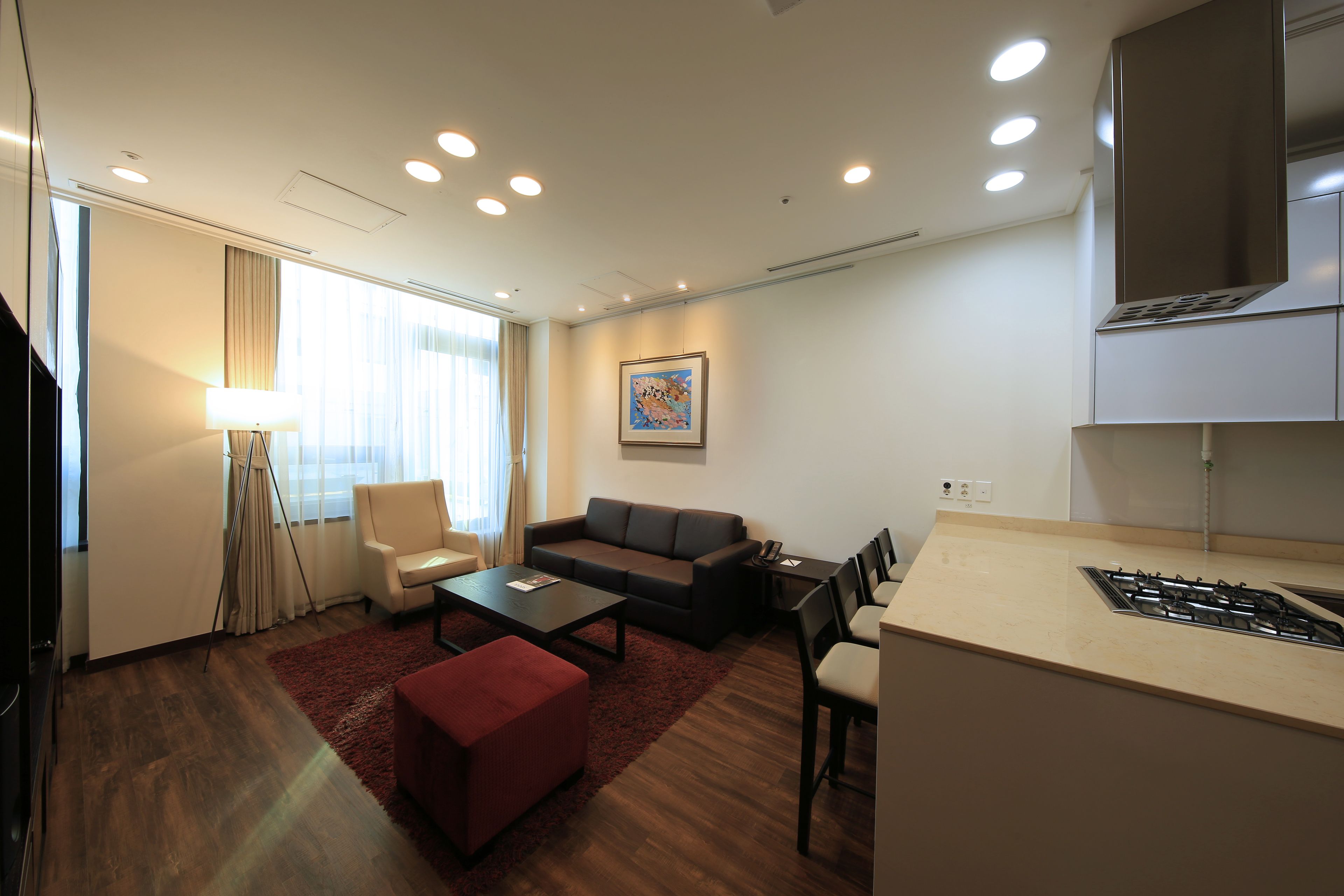 A modern living room with a sofa, coffee table, and ottoman, a dining area with chairs, and a kitchen with a stove.