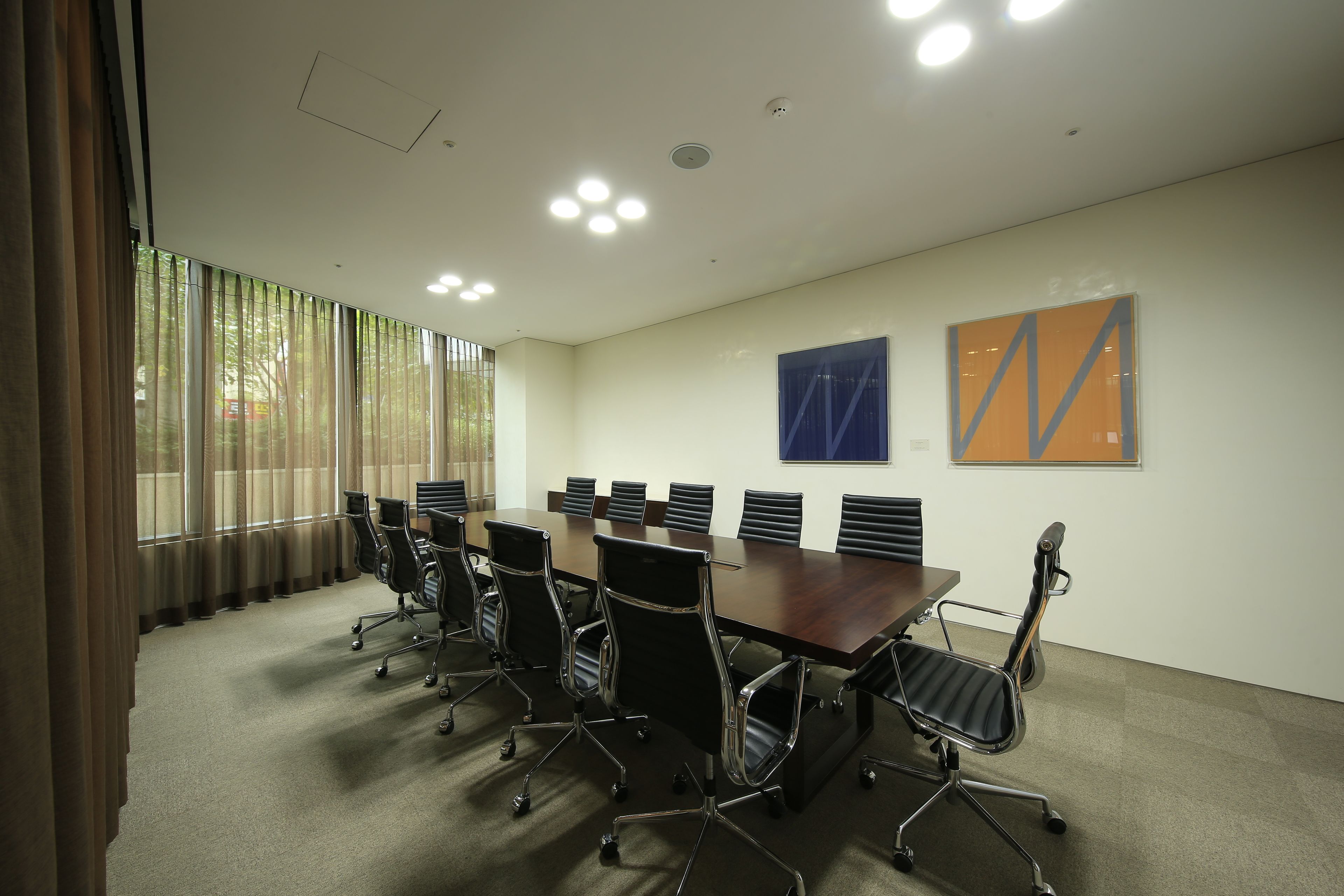 A conference room with a long table, black office chairs, and large windows with curtains.
