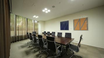A conference room with a long table, black office chairs, and large windows with curtains.