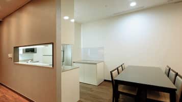 A modern hotel room with a wooden floor, a dining table with chairs, a kitchen area with a microwave, and a large mirror.