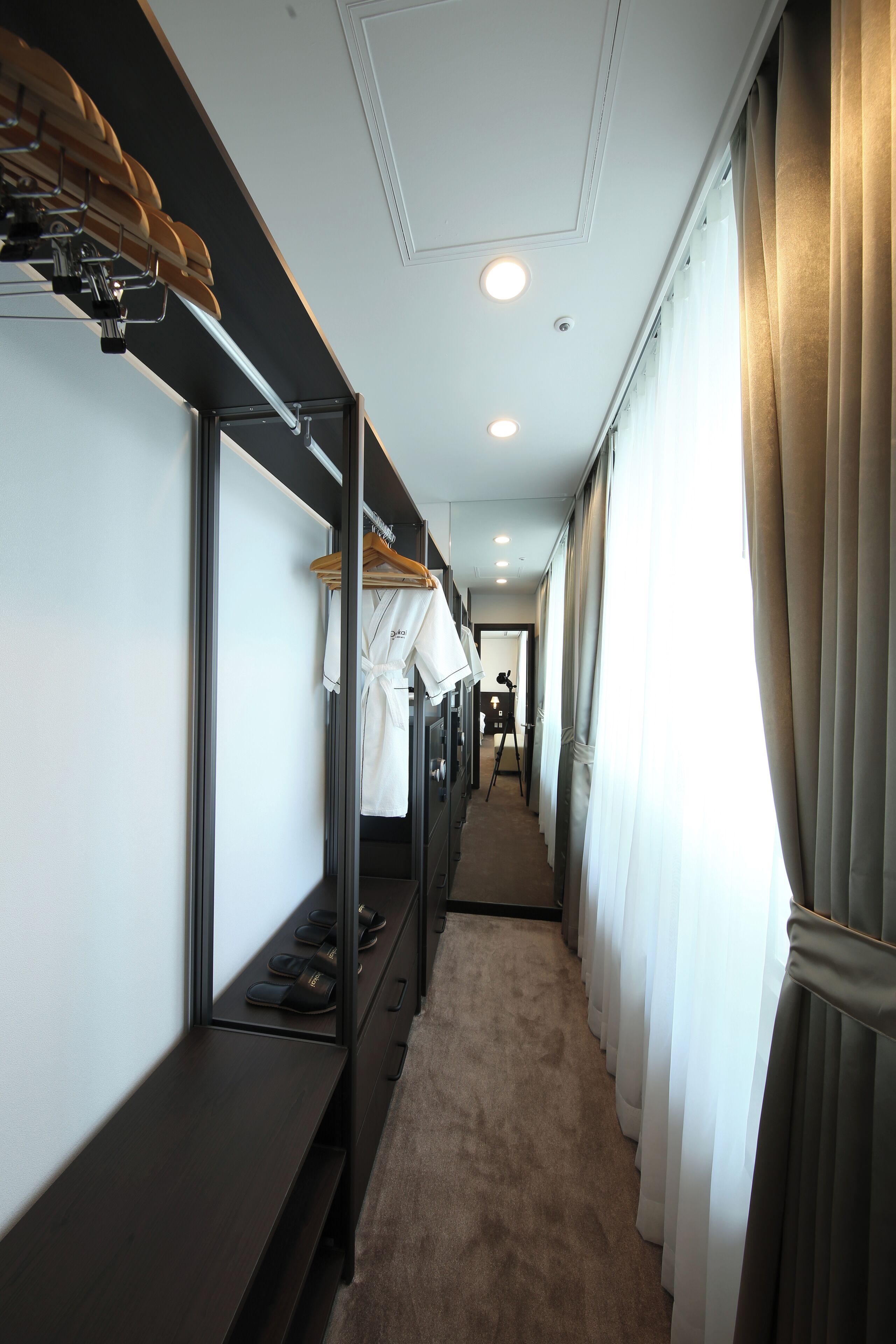 Un couloir d’hôtel avec des lits superposés, un banc avec des chaussures et une vue sur le couloir.