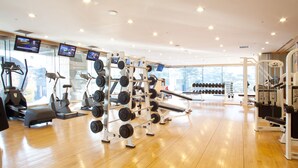 Un gimnasio con máquinas de cardio, equipo de levantamiento de pesas y mancuernas.