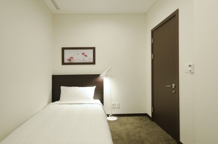 Une chambre d’hôtel avec un lit, une table de chevet, une lampe, une porte et un tableau encadré au mur.
