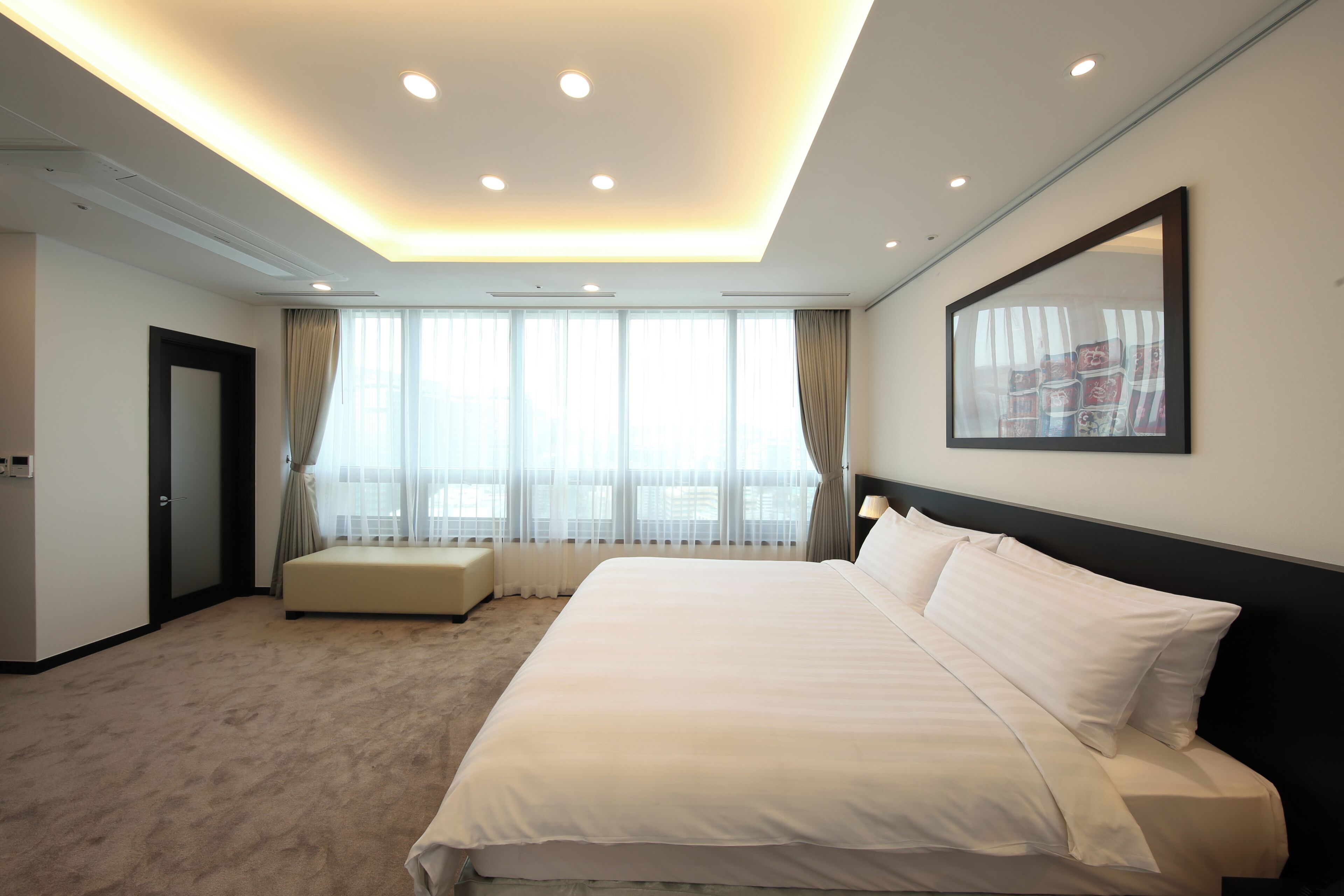 Una habitación de hotel moderna con una cama grande, zona de estar y un ventanal con cortinas.
