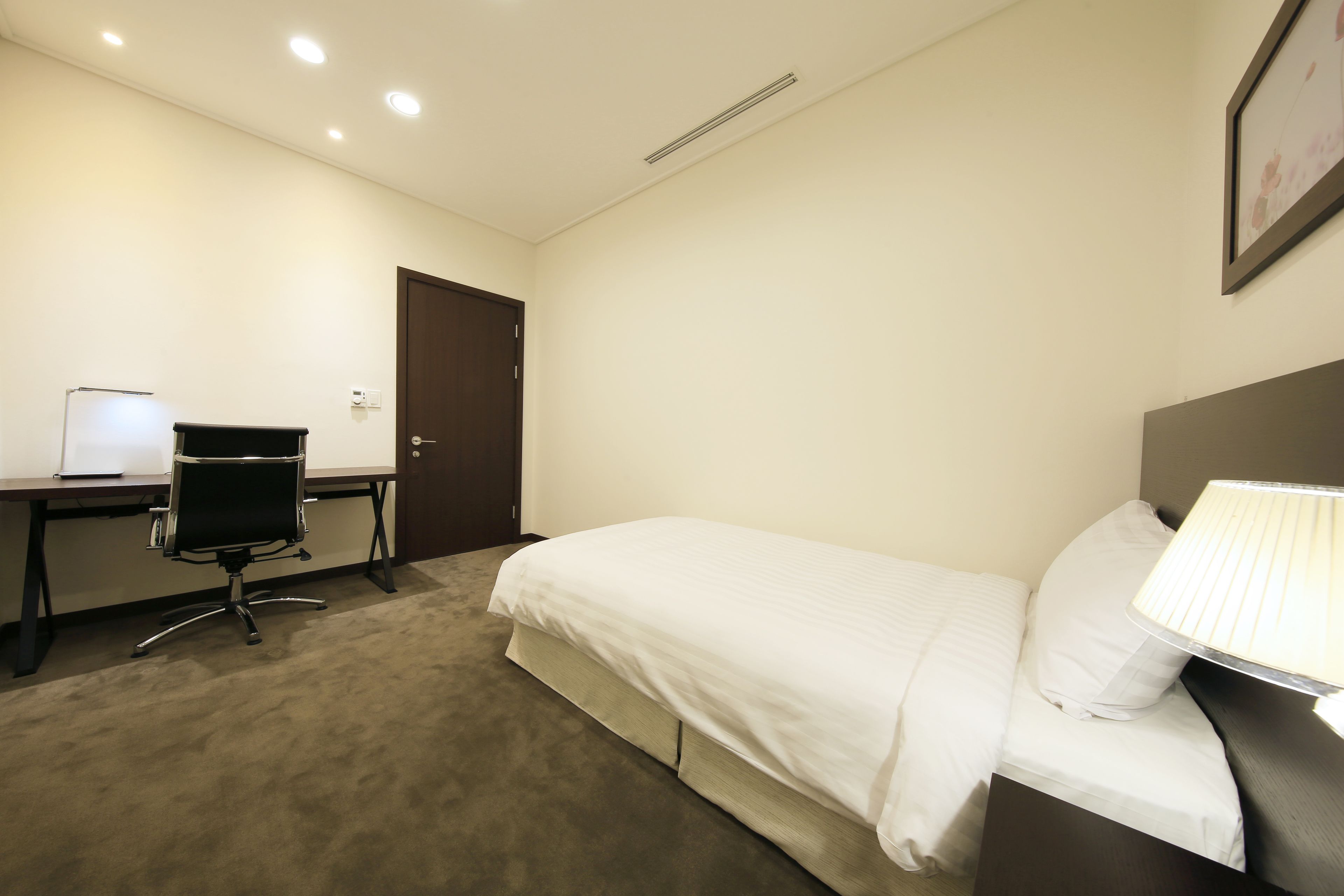 A hotel room with a bed, a desk, a chair, and a lamp.