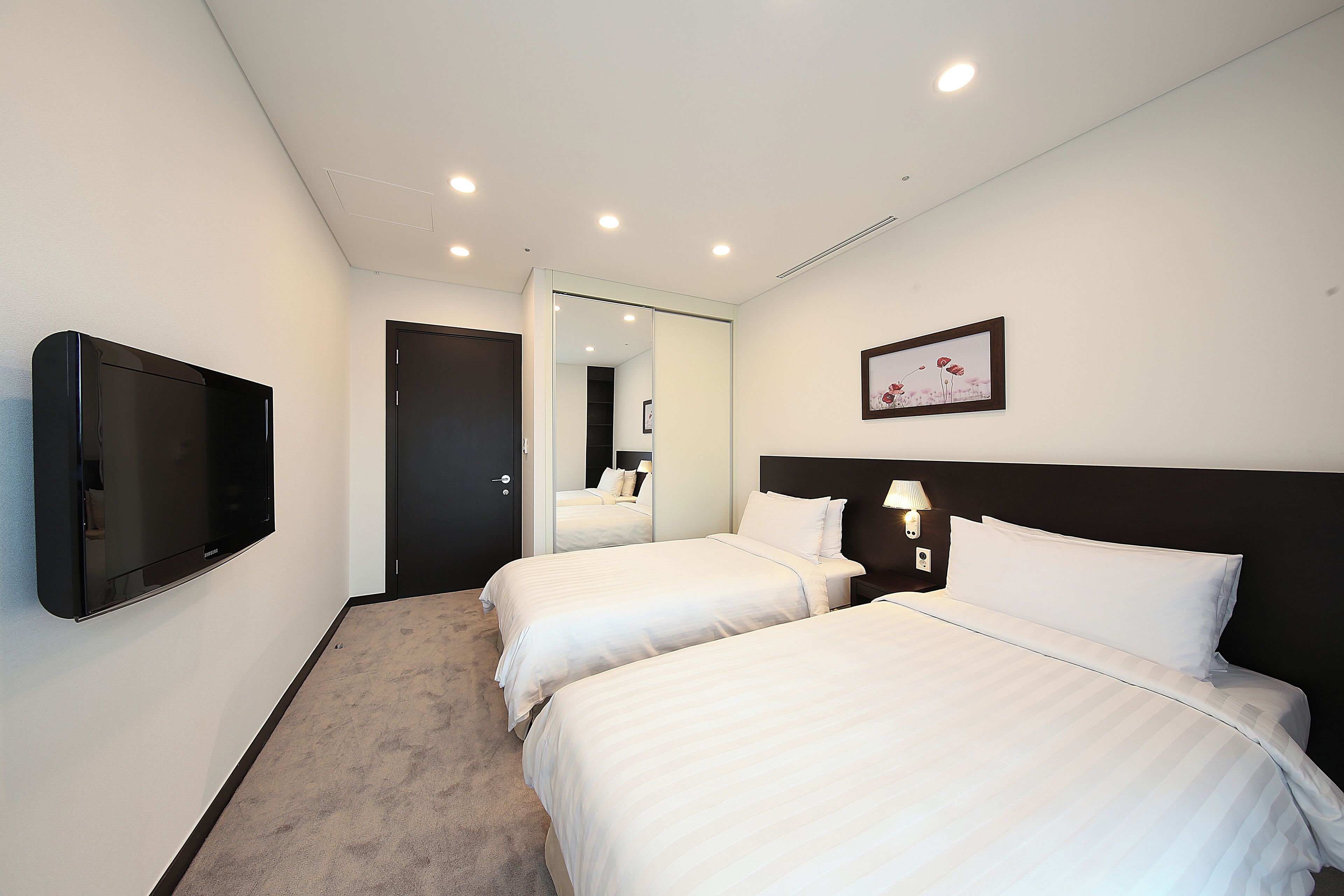 Habitación de hotel con dos camas, un televisor de pantalla plana, un espejo y un cuadro enmarcado en la pared.