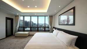 Una habitación de hotel moderna con una cama grande, vistas de la ciudad a través de ventanales del suelo al techo, y un diseño minimalista.