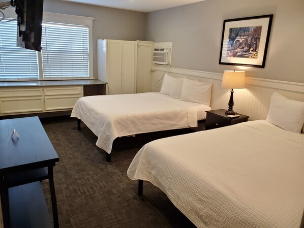 A hotel room with two beds, a desk, a wardrobe, and a window with blinds.
